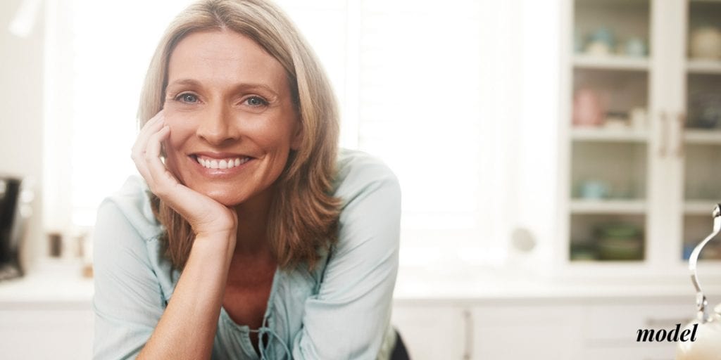 Happy Middle Aged Woman Leaning Over Counter Resting her Chin in her Hand | Westfield Plastic Surgery Center Happy Middle Aged Woman Leaning Over Counter Resting her Chin in her Hand